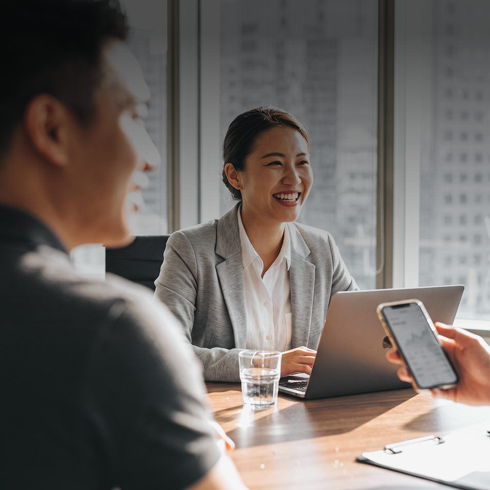 In a meeting room, a smiling woman talks with a colleague across the table