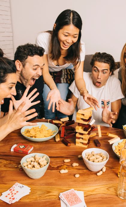 A group of friends playing a block-stacking game around a table, cheering